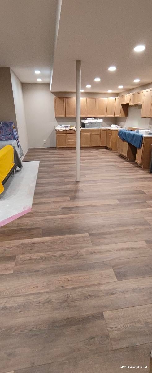 Spacious open-plan kitchen and living area with wood floors, recessed lights, and blue bar stools on the counter.