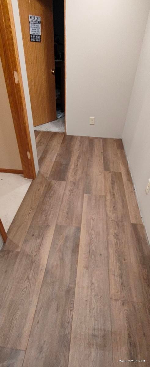 Empty hallway with wood-look flooring, beige walls, and an open doorway on the left.