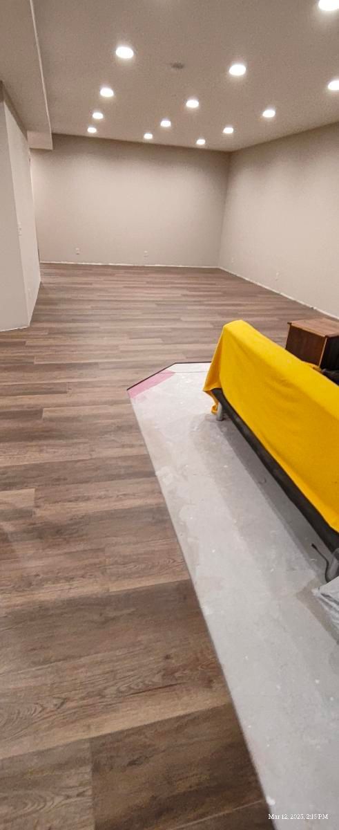 Empty living room with wood floors, recessed lights, and a yellow couch on a rug.