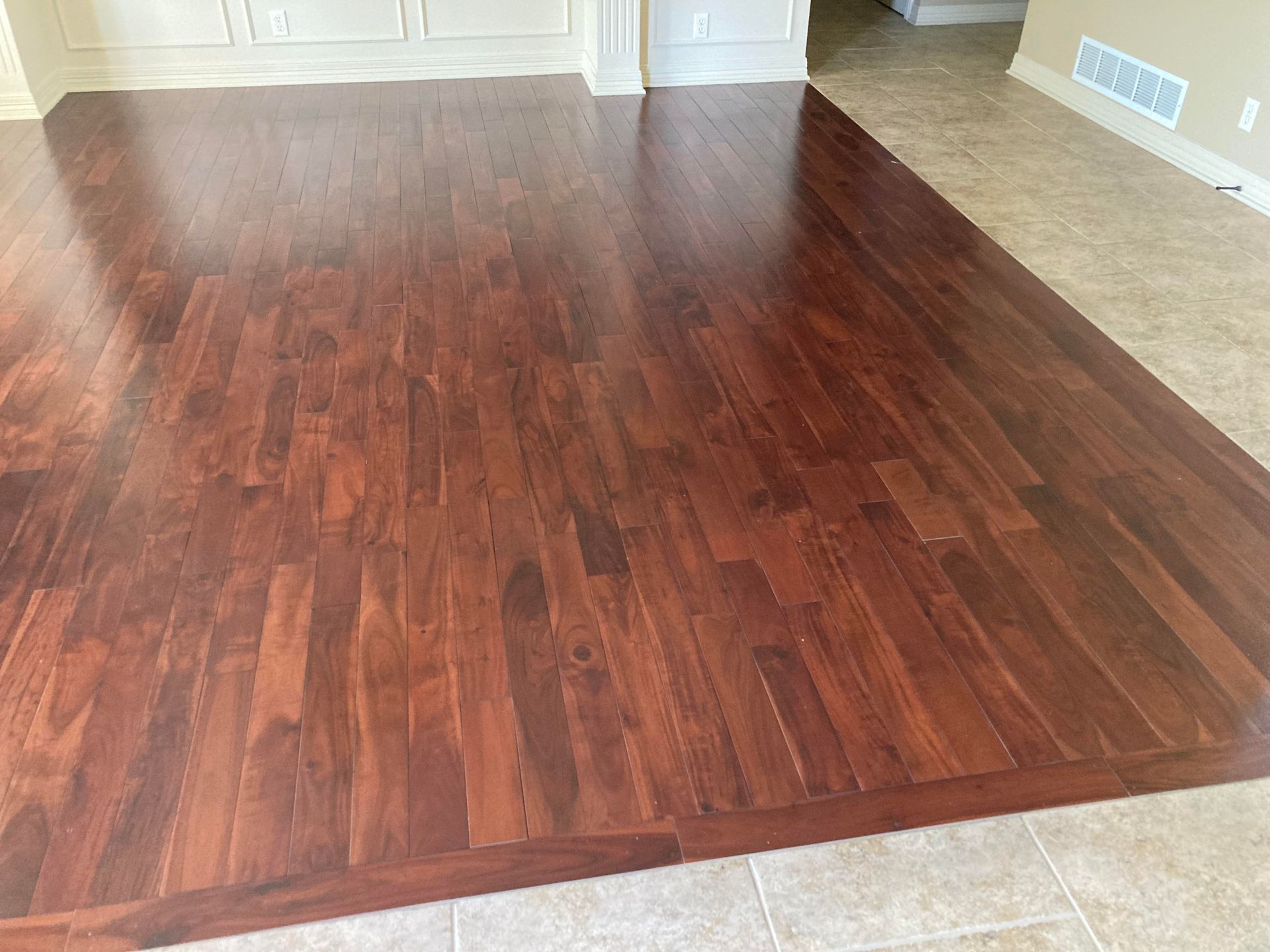 Empty room with dark wood flooring and beige carpet border, viewed from a low angle