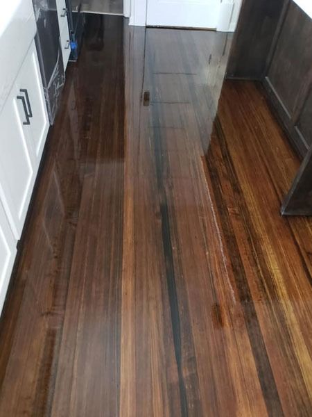 Dark polished wooden hallway with glossy floor, white cabinets on the left, and a doorway at the end.