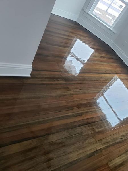 Empty room with glossy dark hardwood floors and sunlight reflecting from two windows.