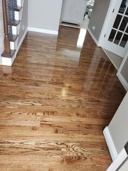 Shiny hardwood hallway floor leading to a doorway, with stairs on the left and white trim walls.