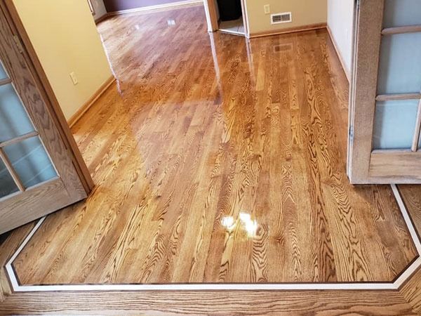 Empty room with glossy hardwood floors and open French doors leading to a hallway