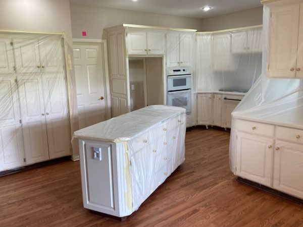Empty white kitchen with an island, built-in ovens, and wood floors