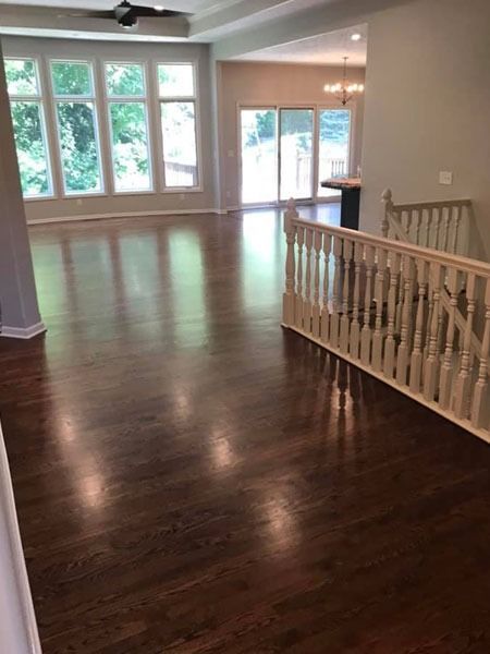 Spacious empty living room with dark hardwood floors, large windows, and a stair railing overlooking the space