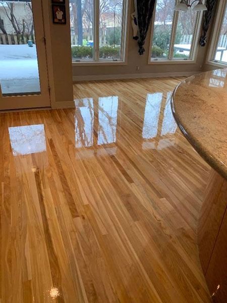 Shiny hardwood floor reflecting windows and a round wooden table in a bright room