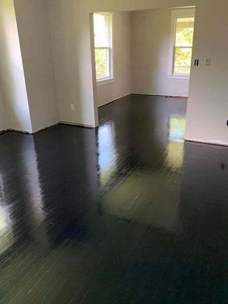 Empty room with glossy black floor and white walls, lit by daylight through windows.