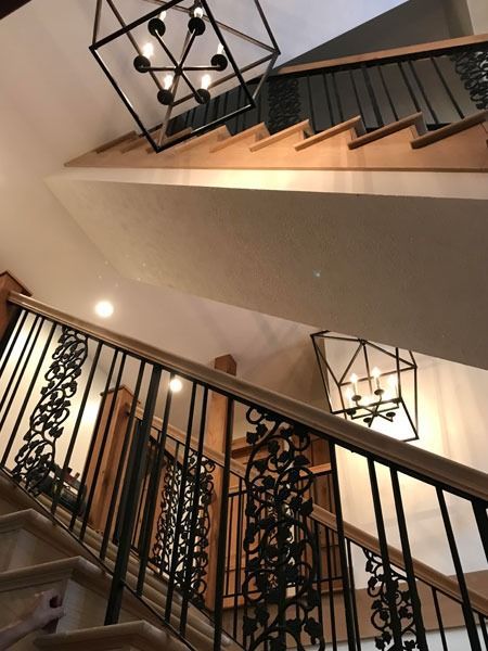Indoor staircase with black railings and modern geometric pendant lights in a warm-toned foyer