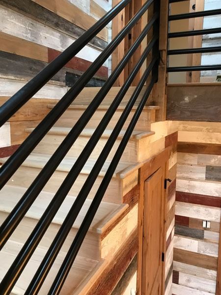 Black metal staircase railing beside a wood-paneled staircase and wall.