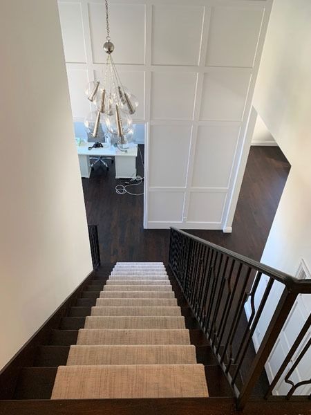 Staircase with dark wood railing leading down to a hallway with white paneled walls and a chandelier.