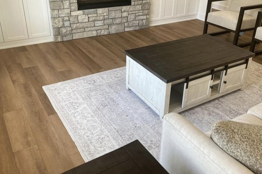 Living room with wood floors, stone fireplace, white rug, and dark coffee table