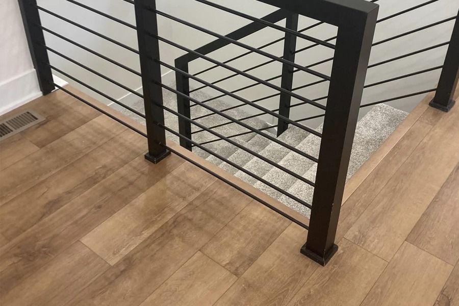 Black metal stair railing over light wood flooring next to carpeted stairs and wall trim
