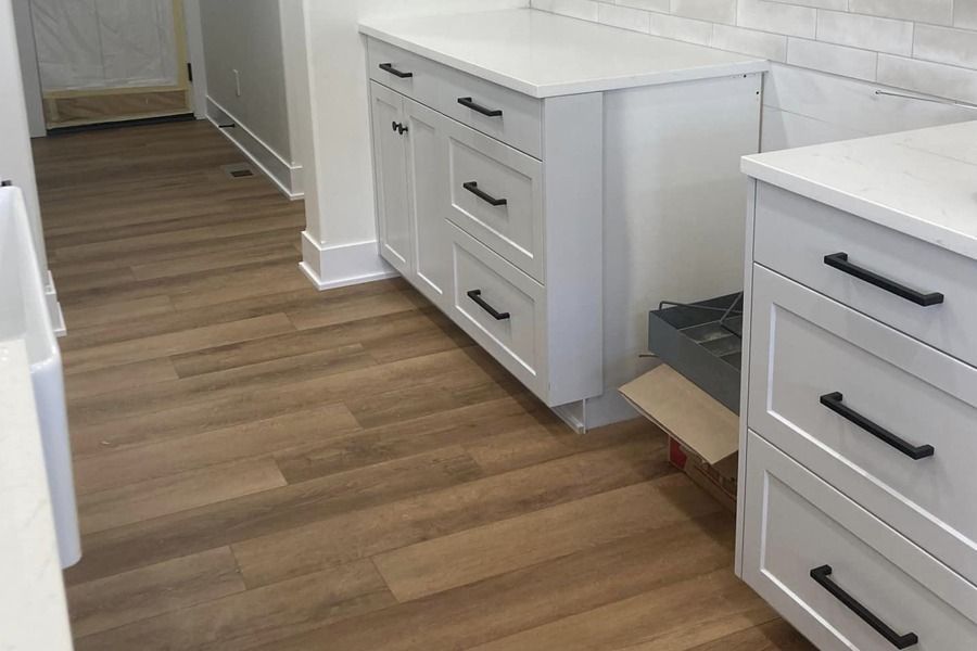 Narrow kitchen hallway with white cabinets and wood-look flooring