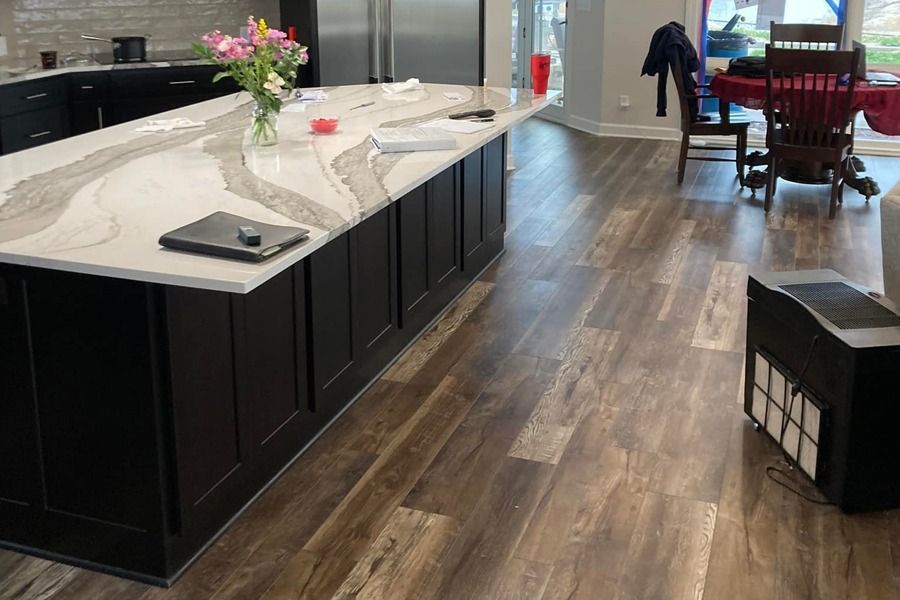 Modern kitchen with white island, dark cabinets, wood floors, and a dining area in the background