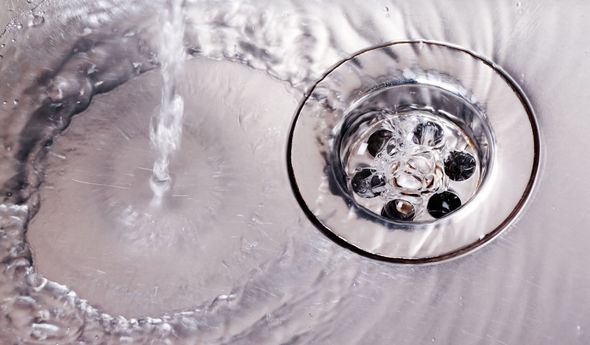 Water flowing into a shiny metal sink drain, creating ripples.