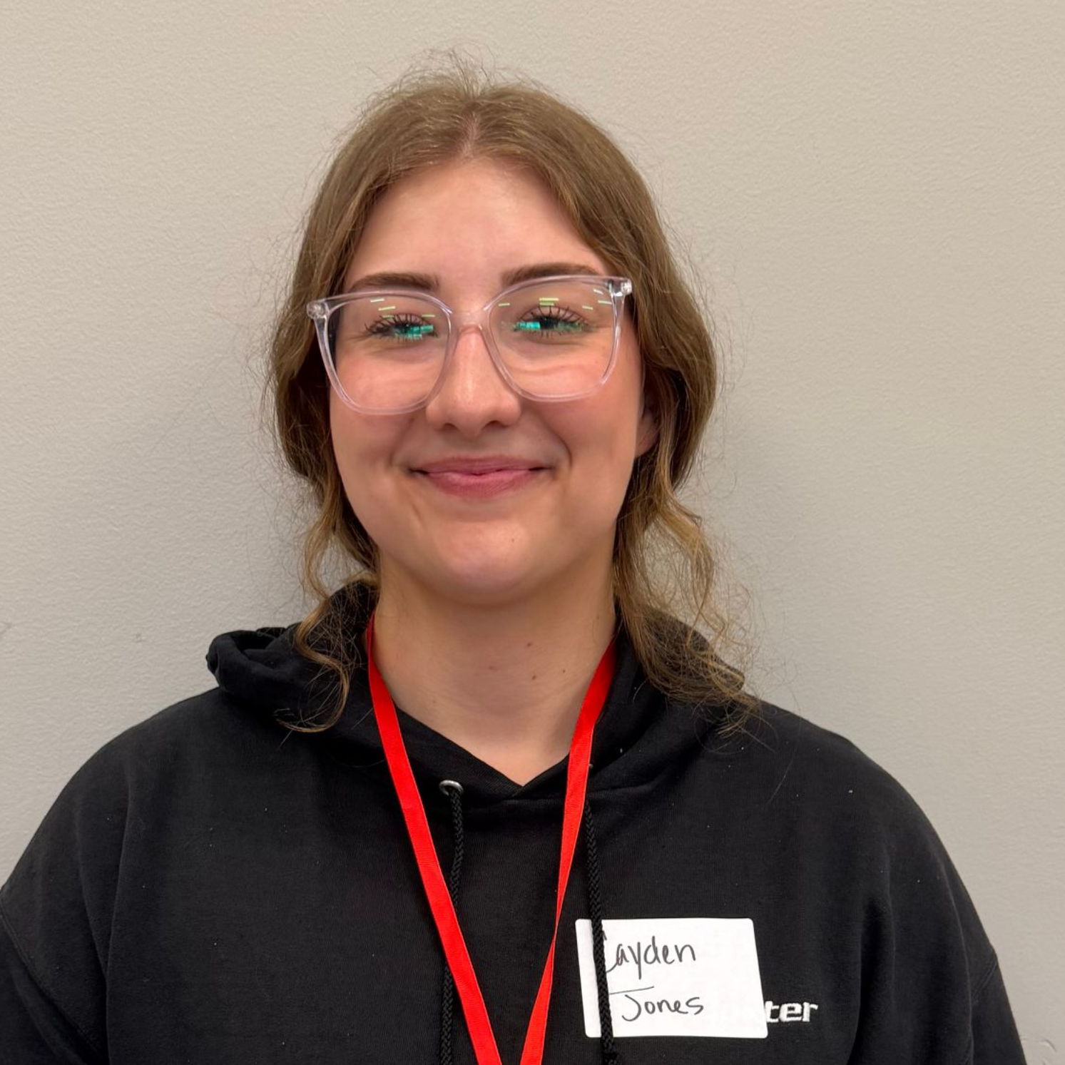 Woman in a blue shirt and tan sweater smiles at the camera, wearing an ID badge.