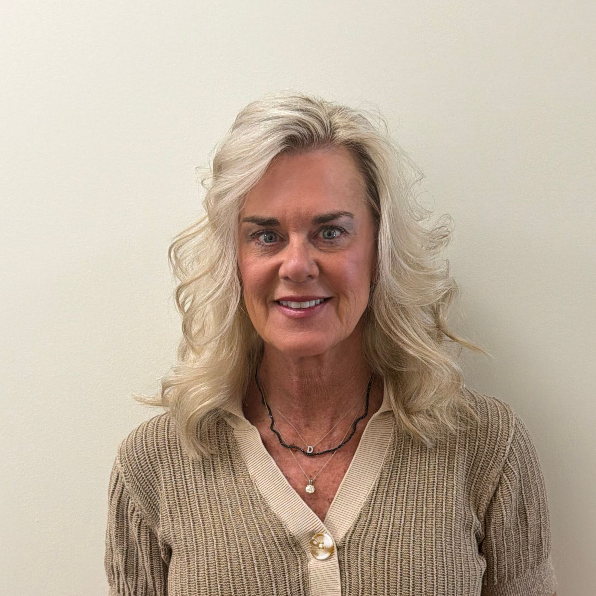 Woman with blonde hair wearing glasses, smiling, wearing a dark top with 