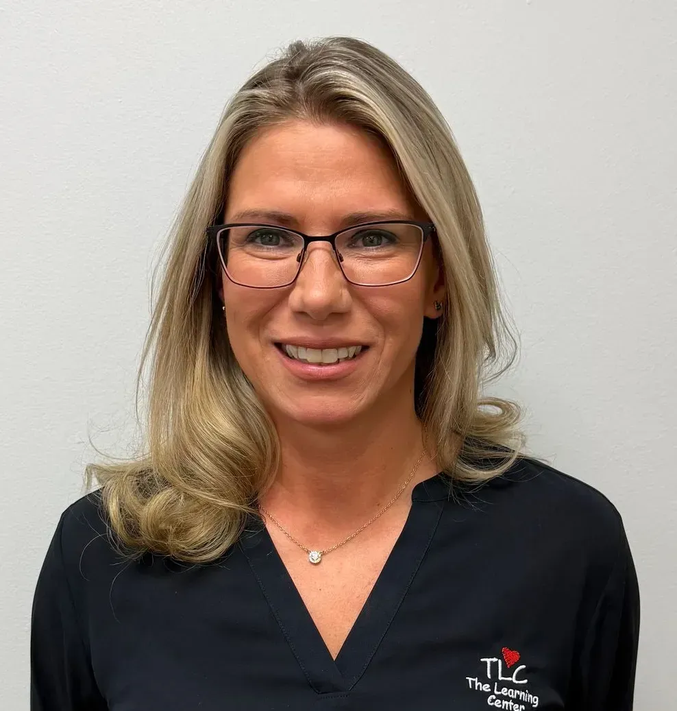 Woman with blonde hair wearing glasses, smiling, wearing a dark top with 