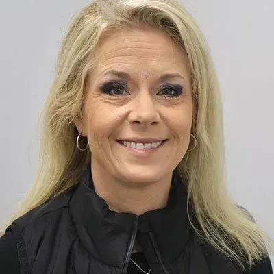 Blonde woman smiling, wearing a black vest and hoop earrings, against a white background.