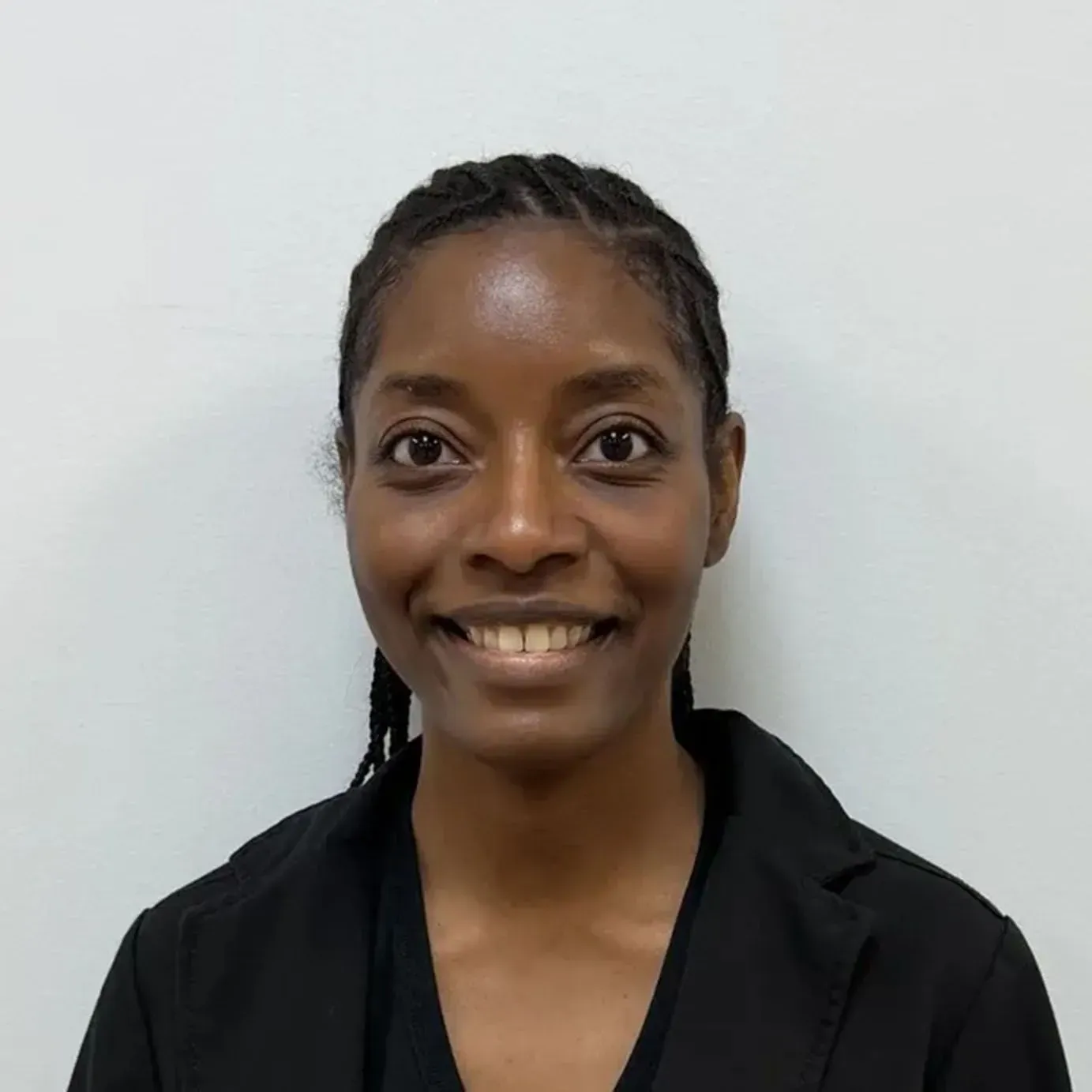 Woman with dark skin, smiling, wearing a black blazer. Braided hair, against a white background.