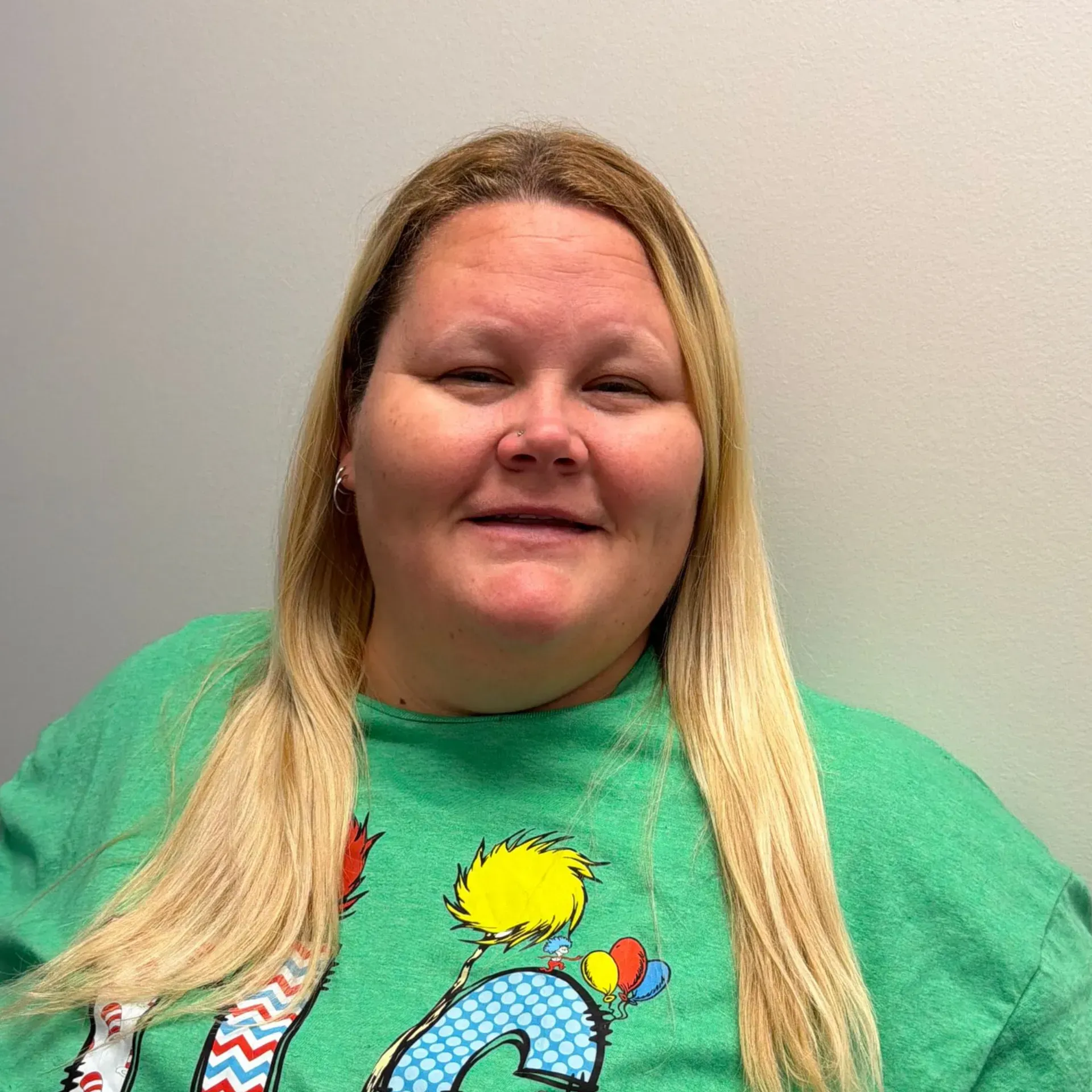 Woman with blonde hair wearing a green shirt smiling, sitting in front of a neutral wall.