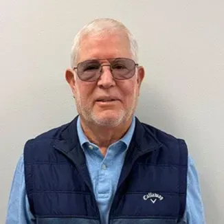 Man wearing glasses and vest, looking forward against a gray background.