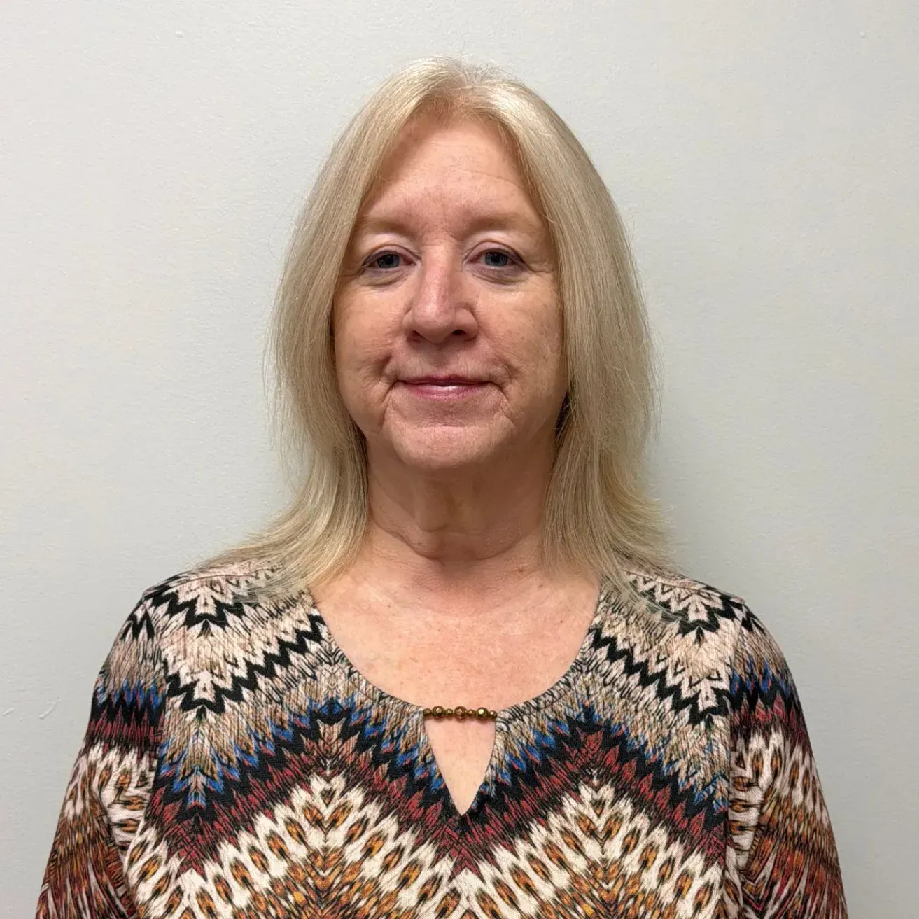 Woman with blonde hair, wearing a patterned top, looking directly at the camera.