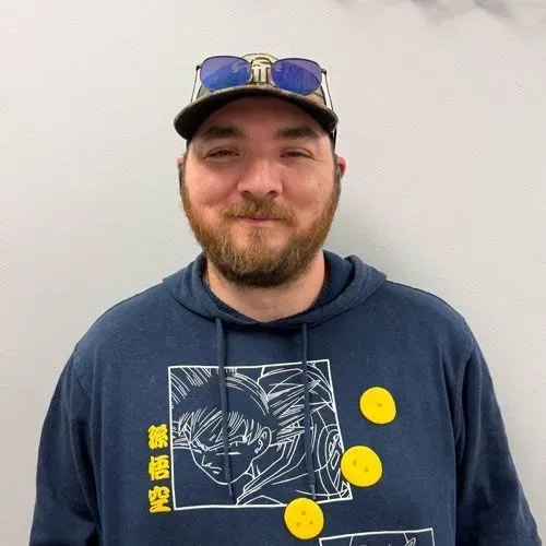 Man wearing a hat and hoodie with cartoon graphic and three yellow circles attached. Smiling, looking at camera.