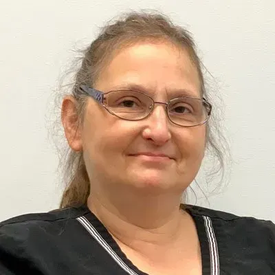 Woman with glasses smiling, wearing a black top against a white background.