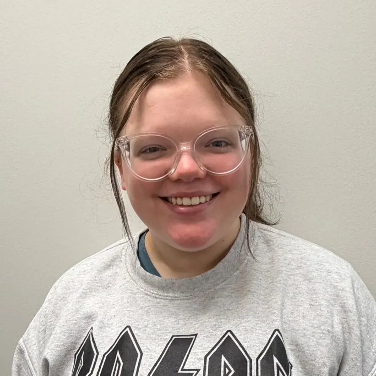 Smiling person wearing clear glasses and a gray sweatshirt.