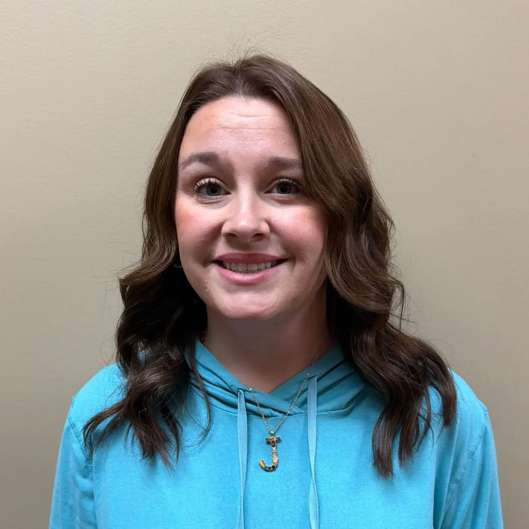 Woman in blue hooded sweatshirt smiles at the camera against a neutral background.