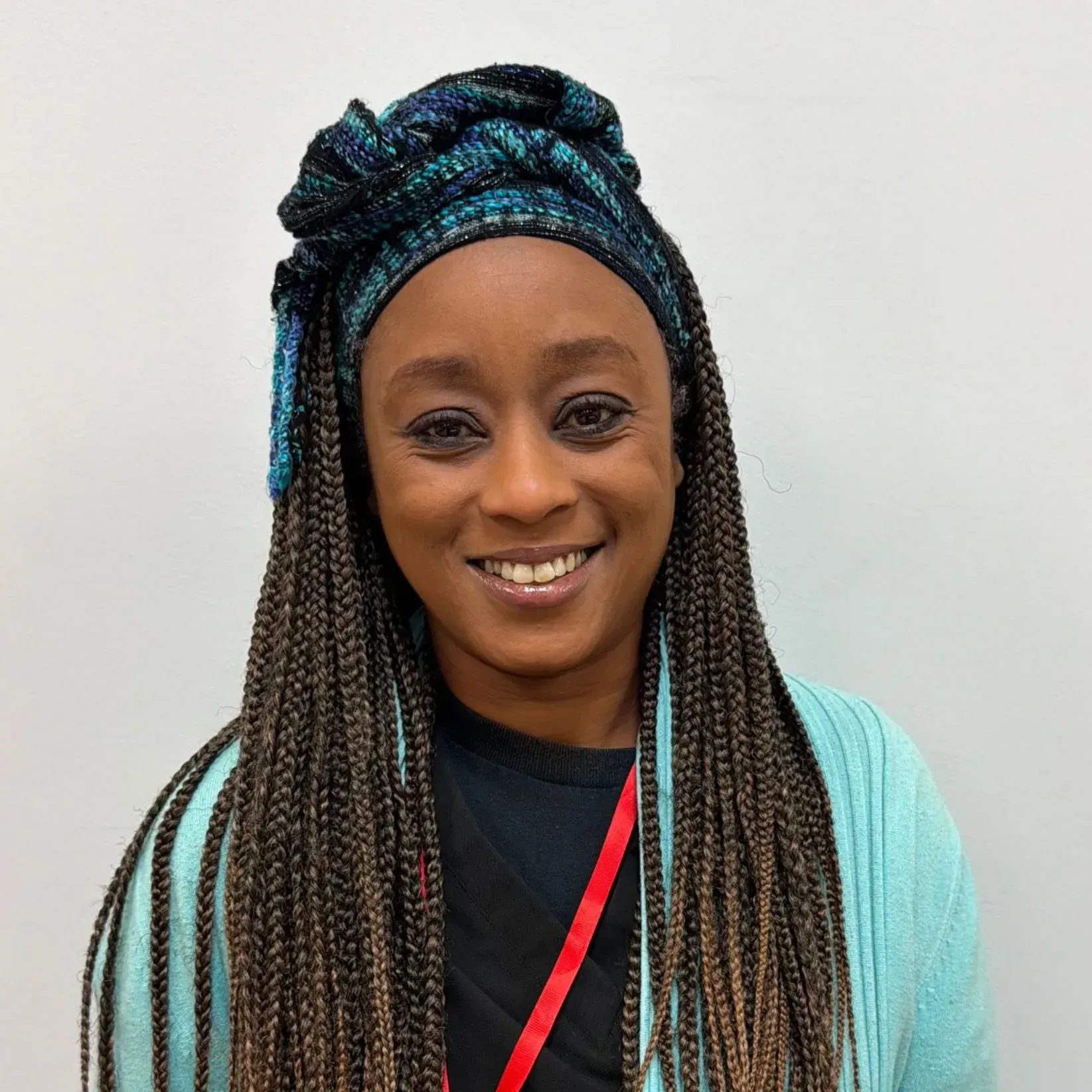 Woman with long, braided hair, wearing a patterned head wrap and light blue cardigan, smiles at the camera.