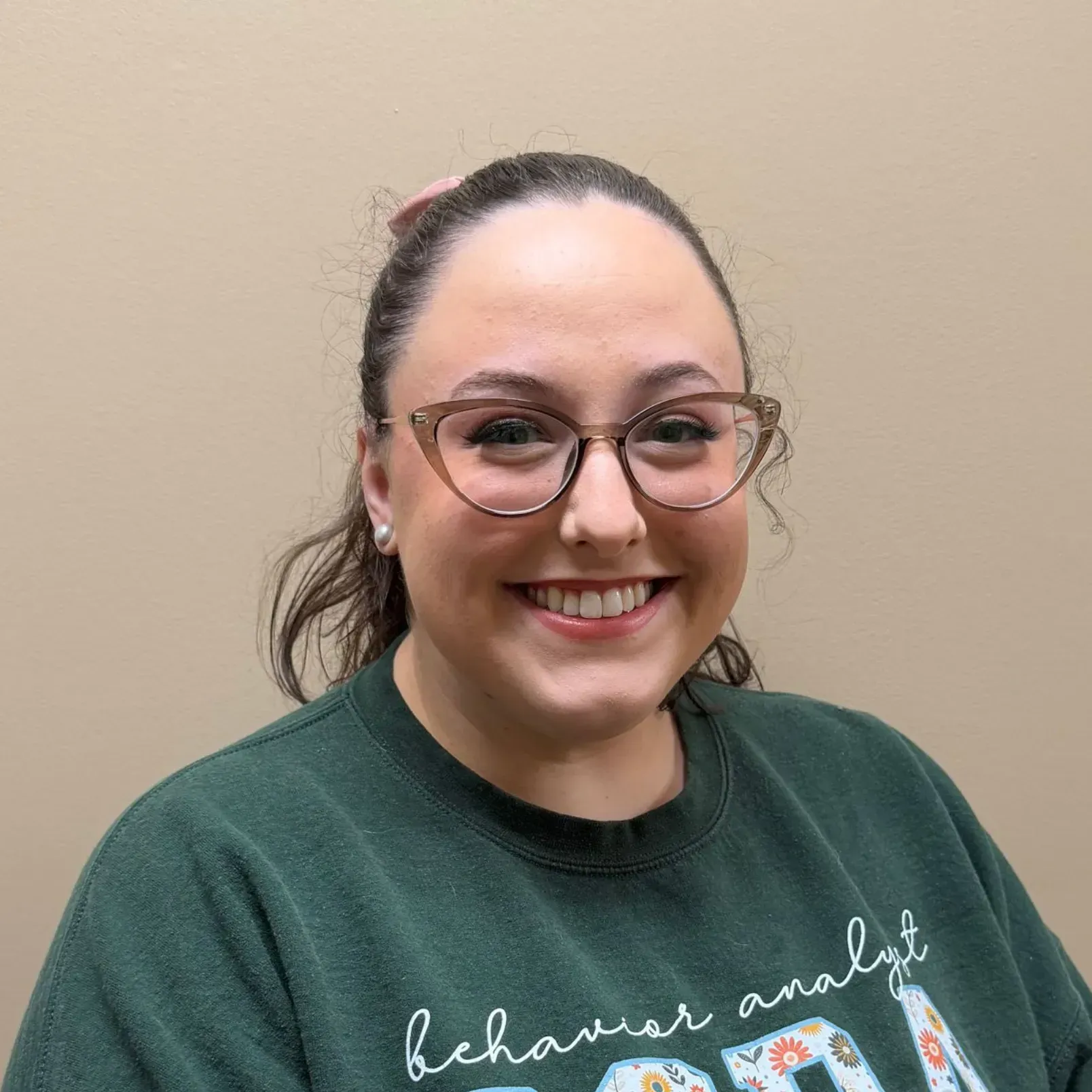 Woman with glasses smiles; wearing a green sweatshirt that says 