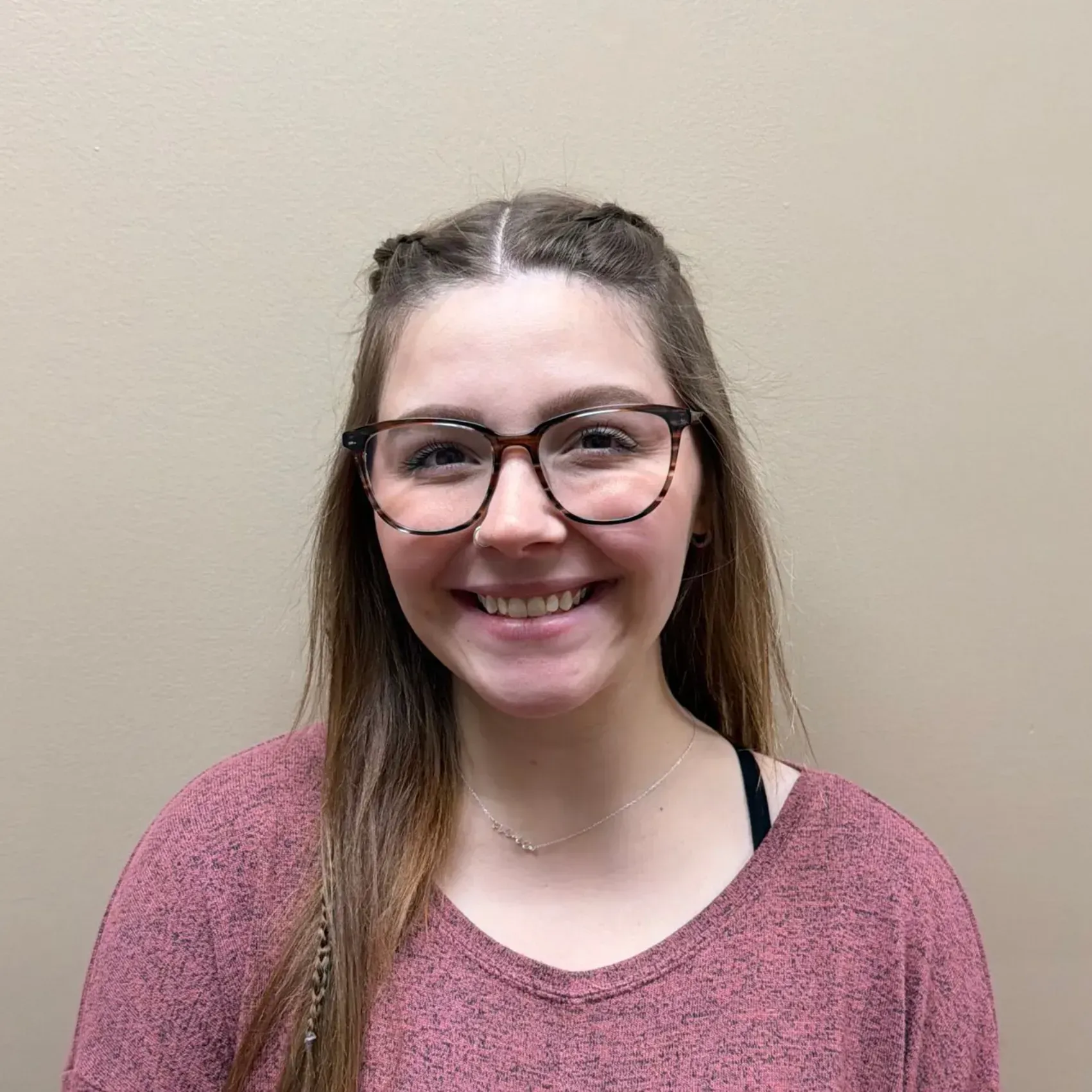 Woman with glasses smiles; wearing a pink sweater.