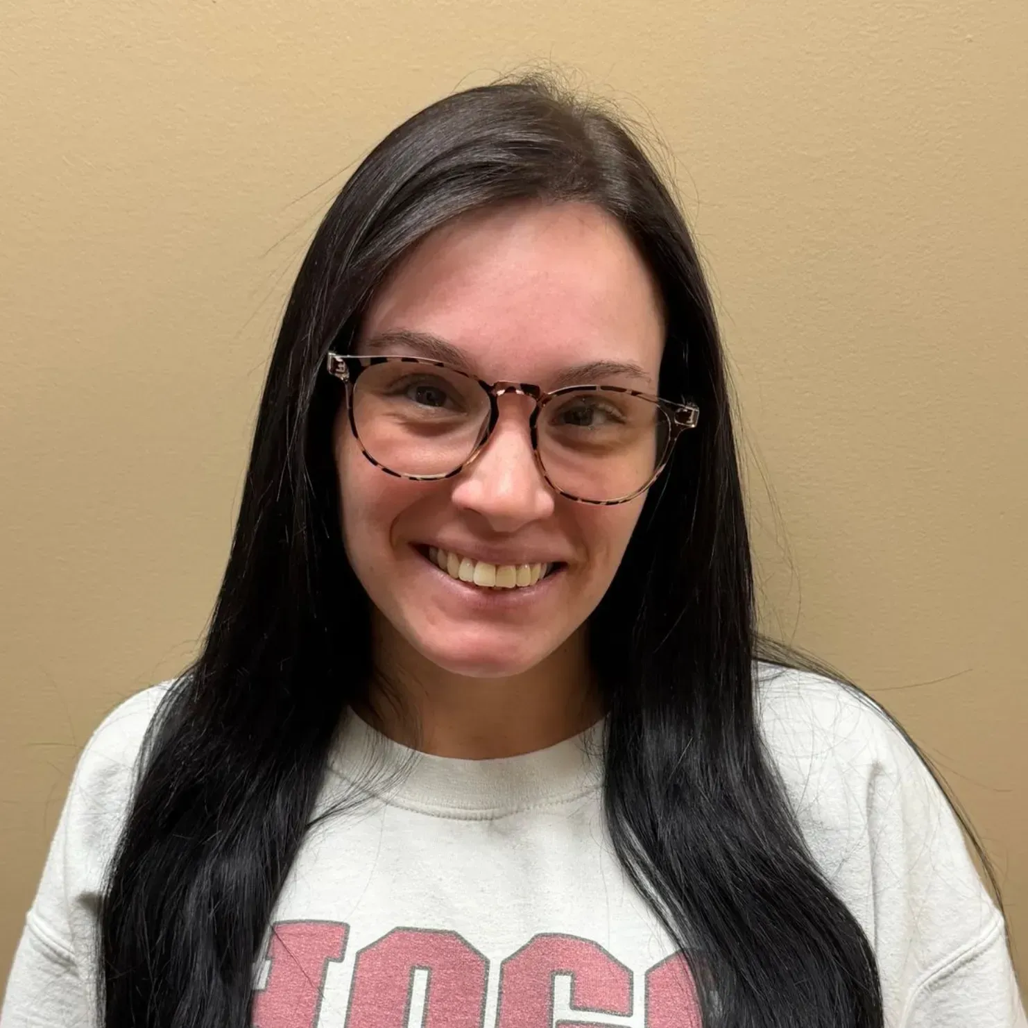 Woman with dark hair and glasses smiles at the camera, wearing a white sweatshirt.