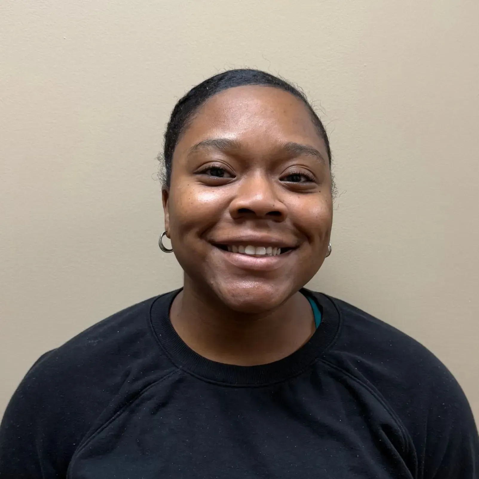Smiling person in black shirt, small hoop earrings, and neutral background.