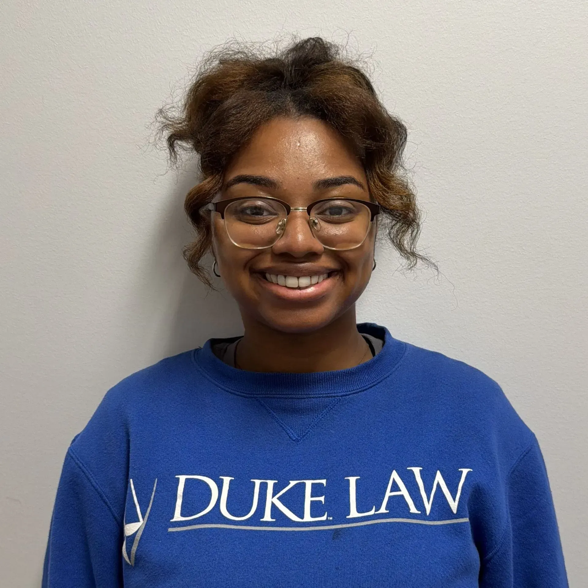 Person wearing glasses and a blue Duke Law sweatshirt smiling. Against a white wall.
