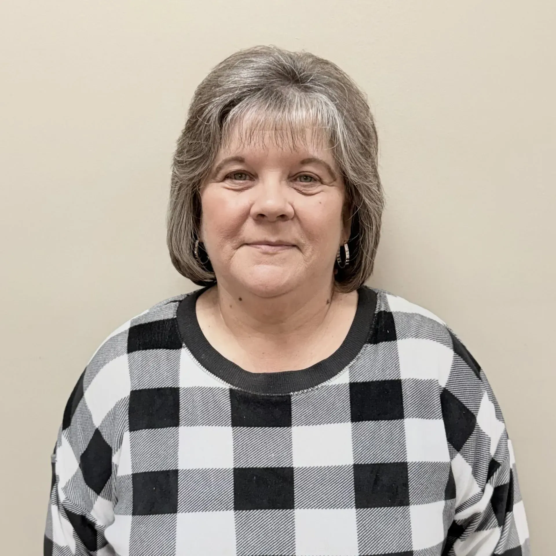 Woman wearing a black and white plaid sweater smiles in front of a neutral-colored wall.