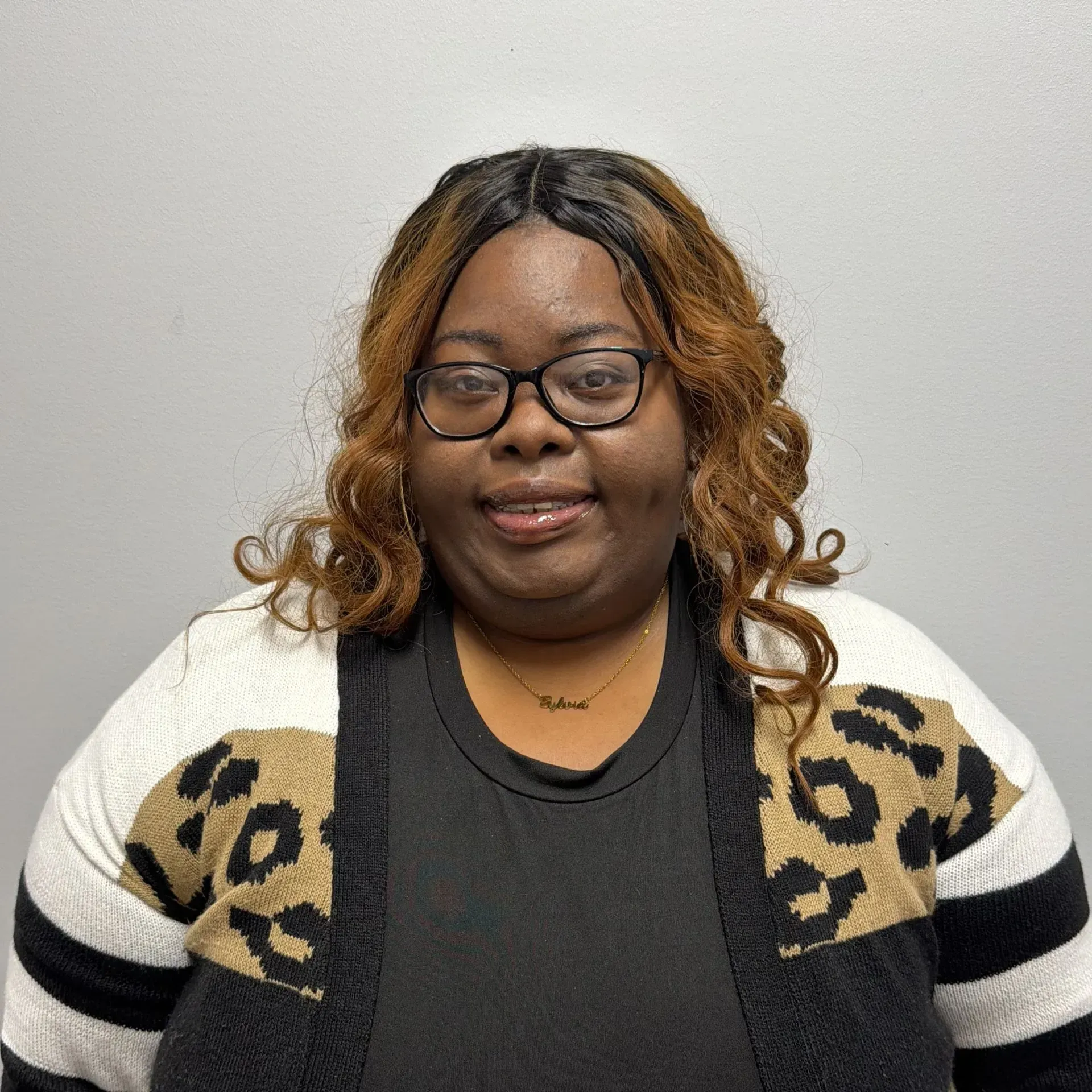 Person wearing glasses and a patterned sweater smiles at the camera against a plain background.