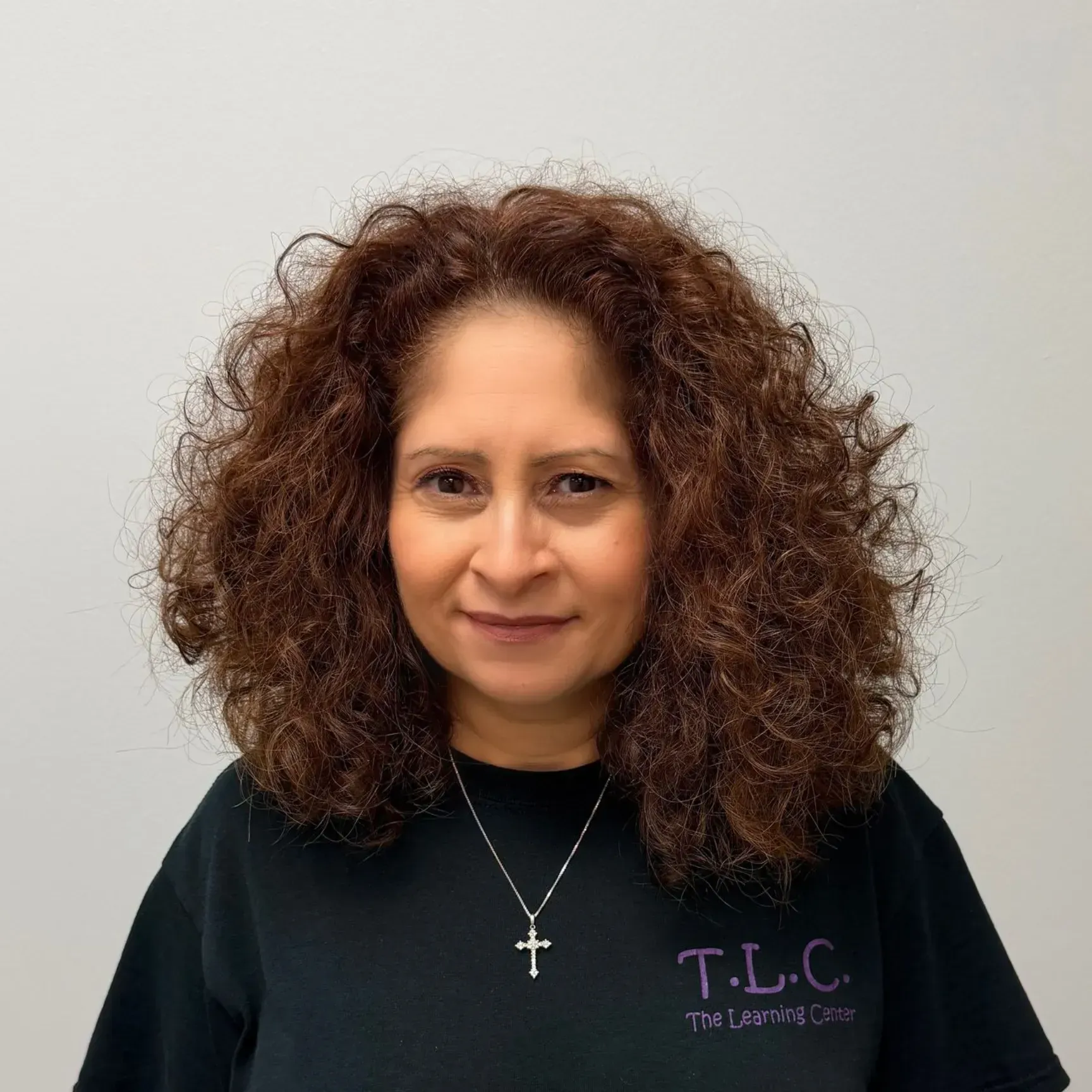Woman with curly brown hair, wearing a black shirt with a cross necklace, smiling at the camera.