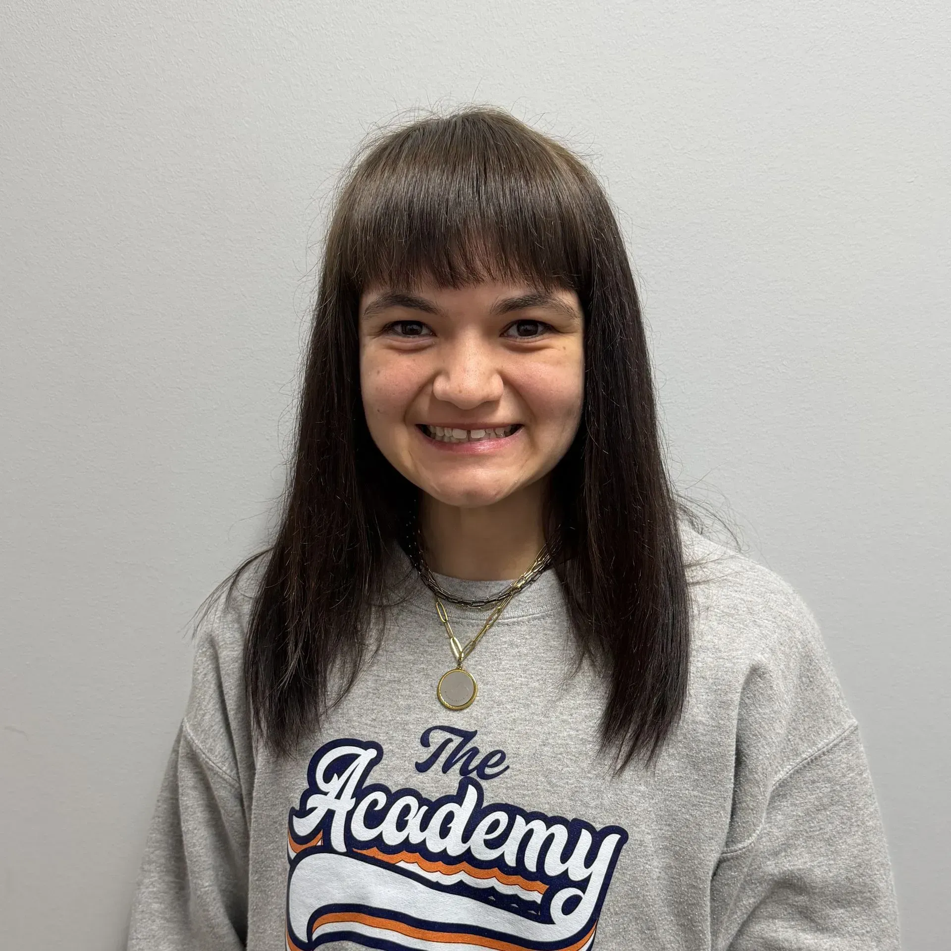 Woman with bangs, wearing a gray sweatshirt with 