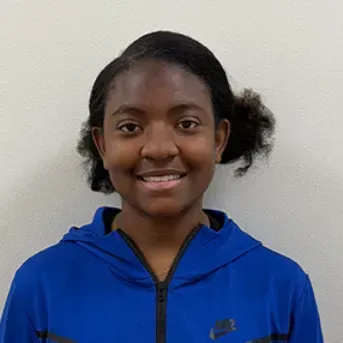 Person in a blue zip-up jacket smiles at the camera against a neutral background.