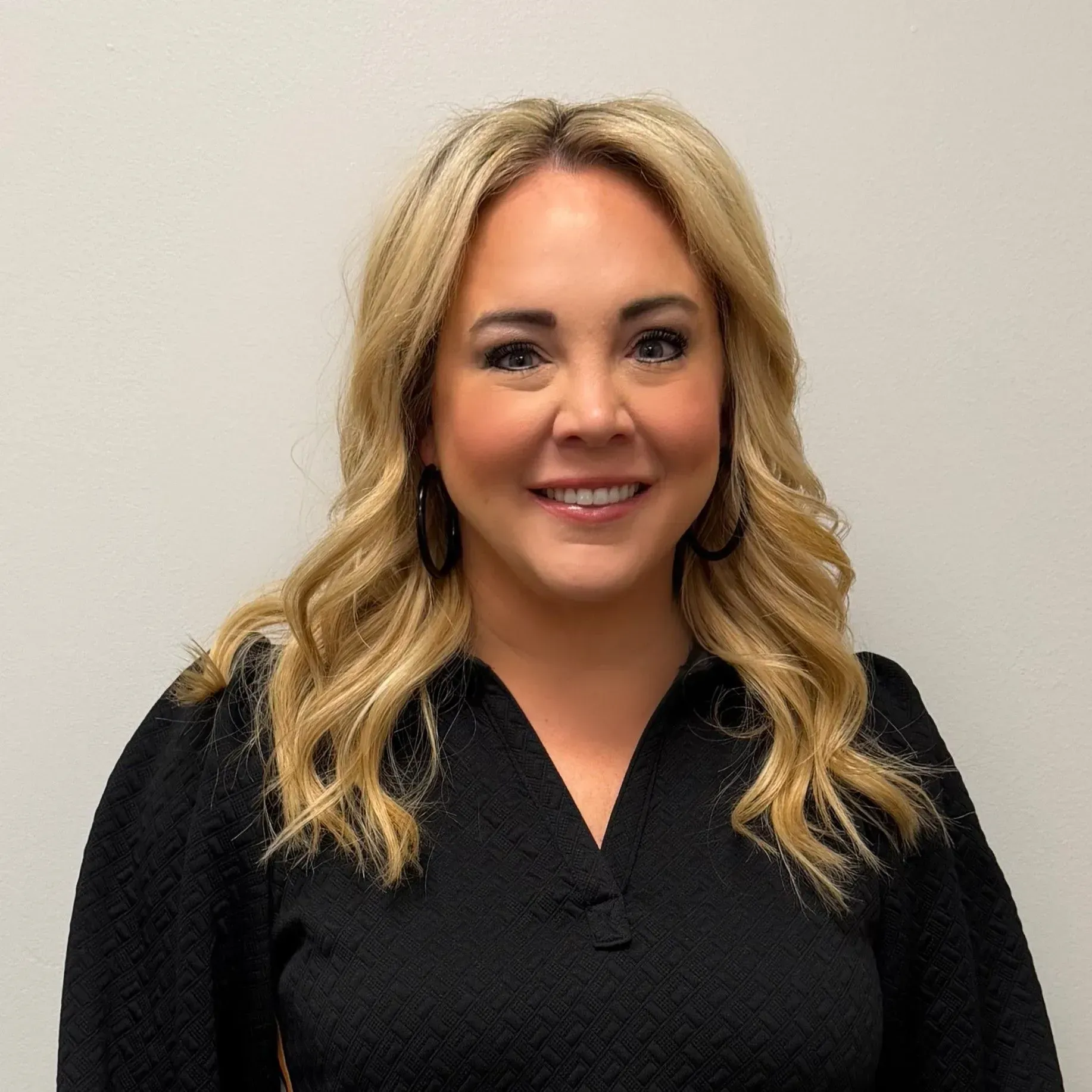 Woman with blonde wavy hair, wearing black top, smiling.