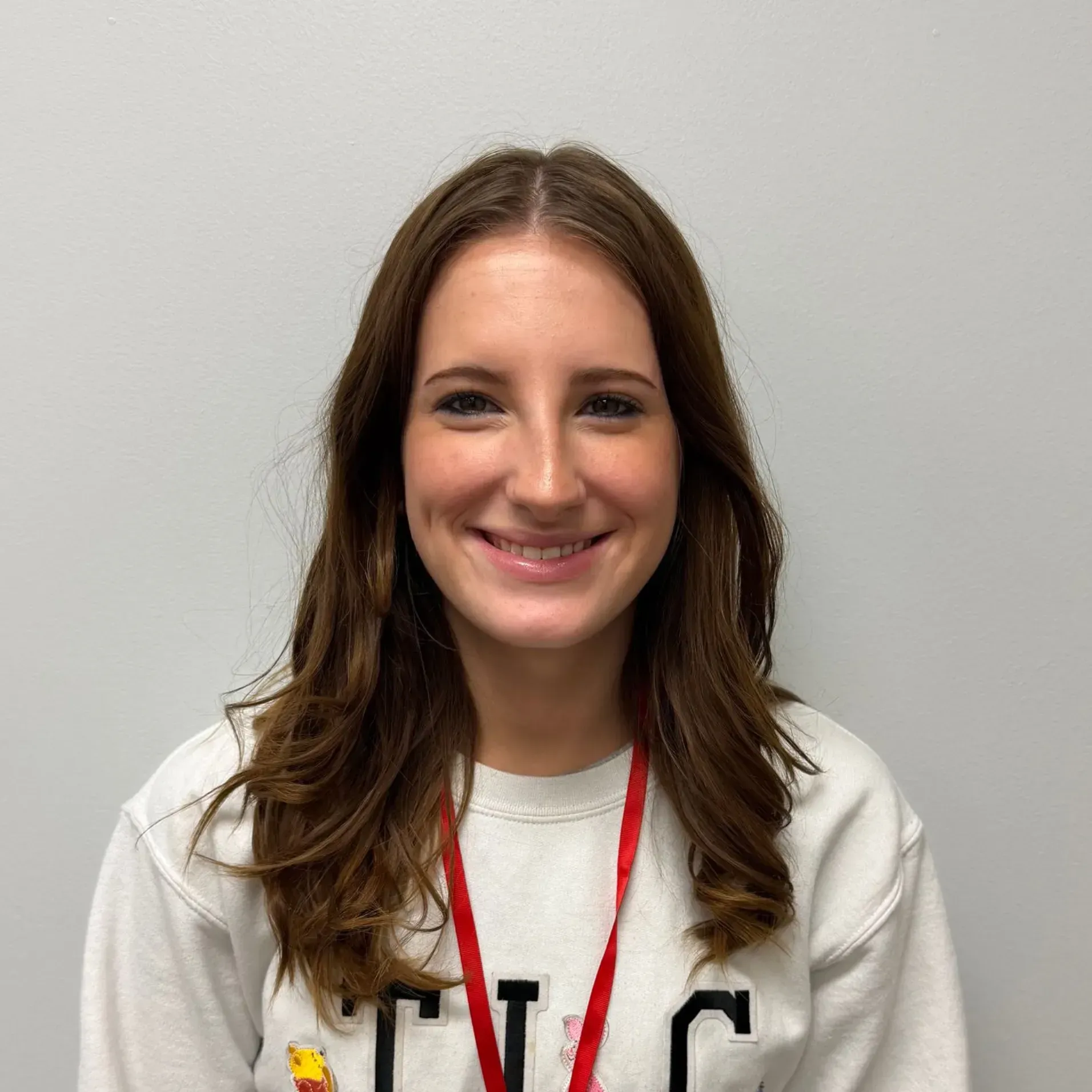 Woman smiling, wearing a white sweatshirt, red lanyard; light gray background.