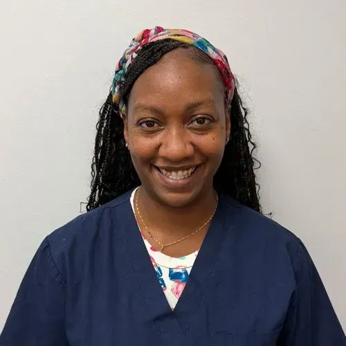 Woman with braided hair, smiling, wearing a patterned headband and a blue top over a floral shirt.