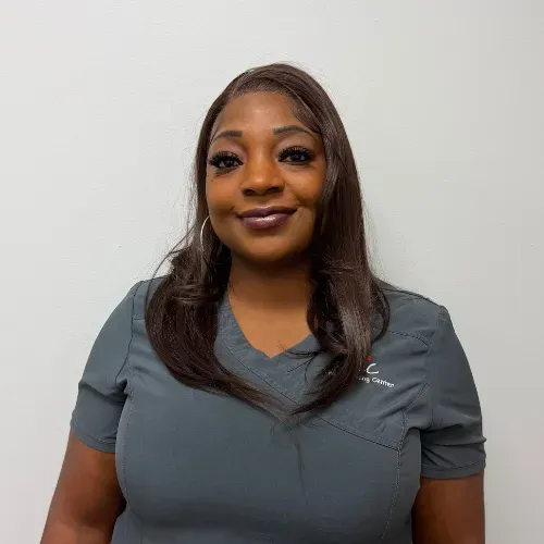 Woman in gray scrubs smiles at the camera, posing against a white background.