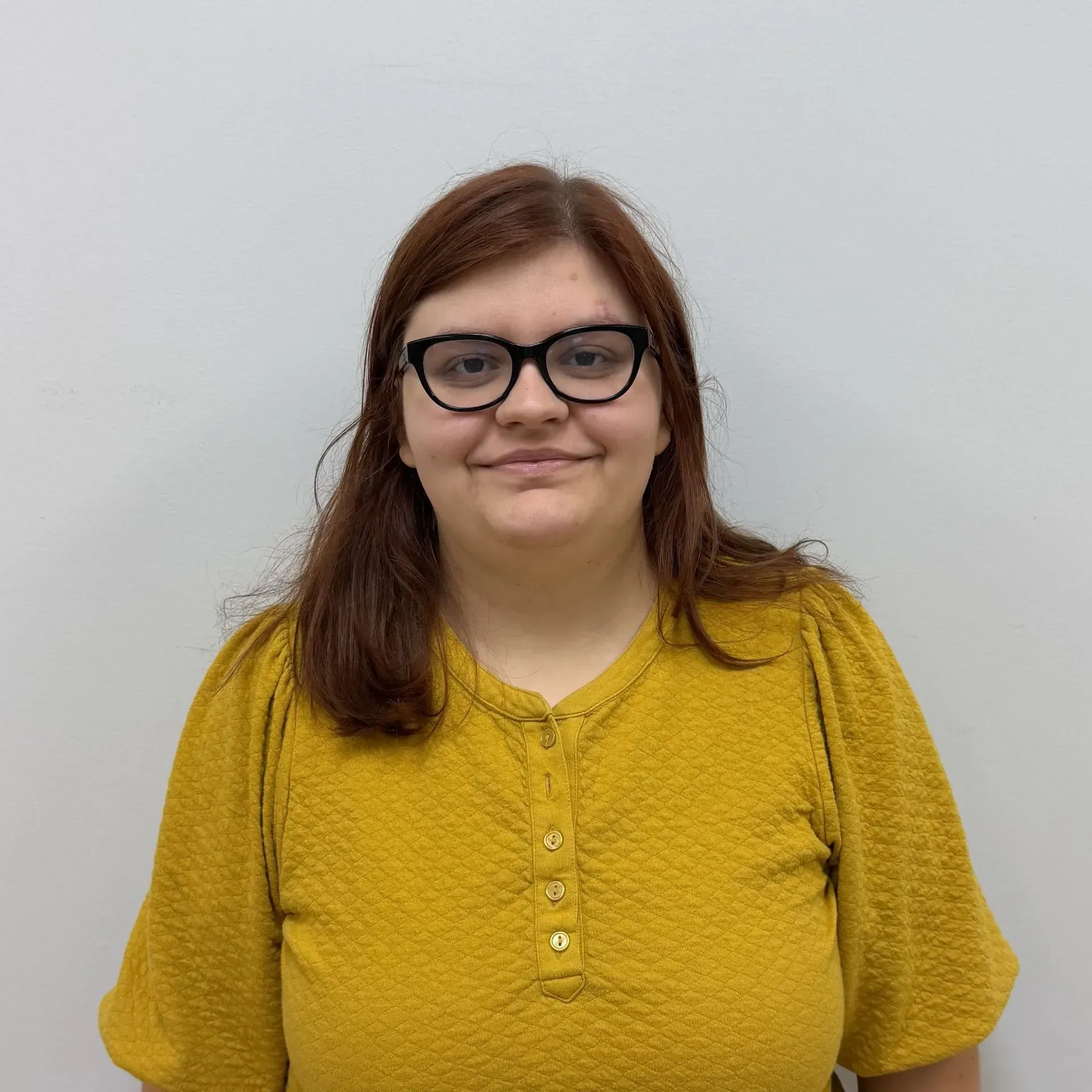 Woman wearing glasses and a yellow shirt, smiling against a white background.