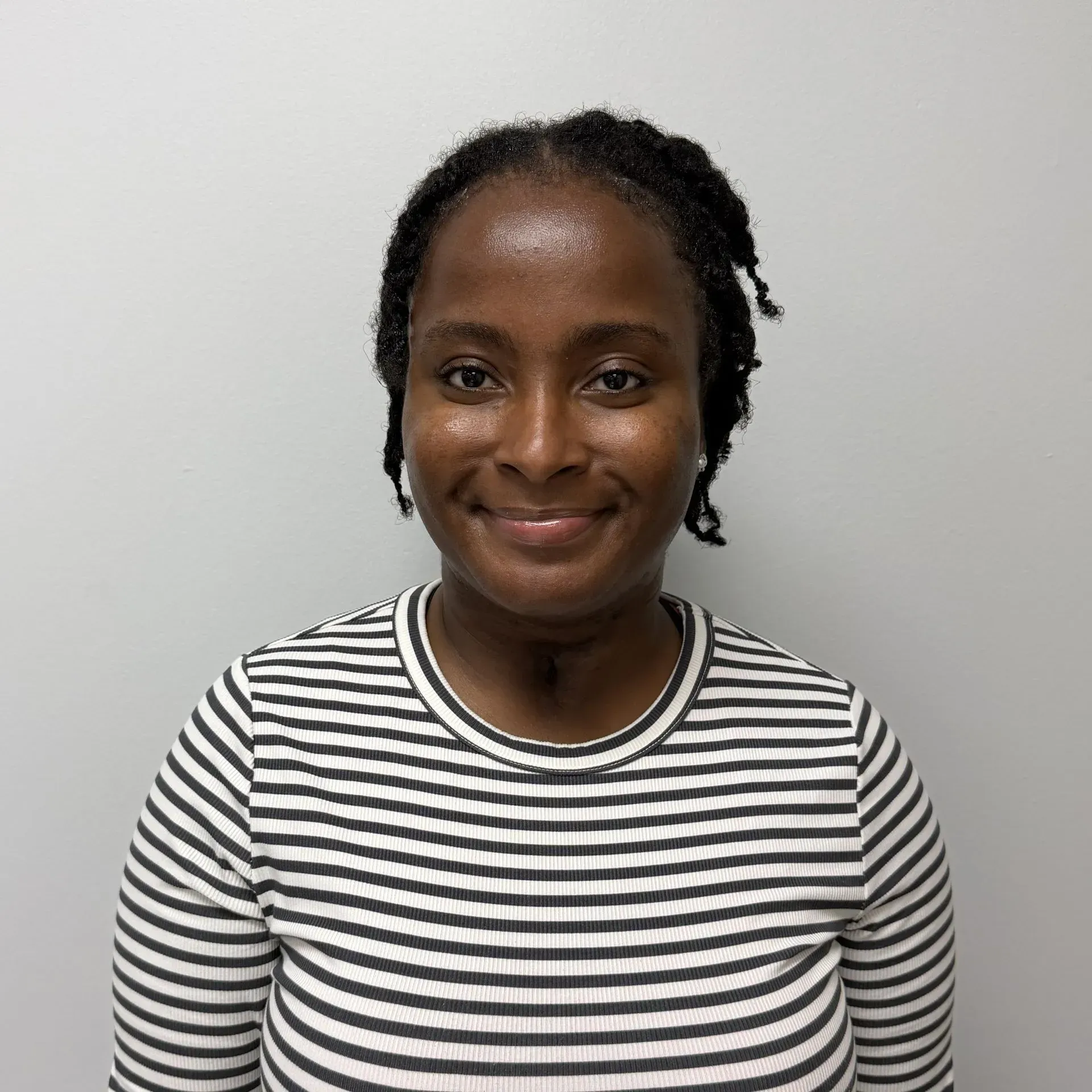 Woman with dark hair in a striped shirt, smiling in front of a gray wall.