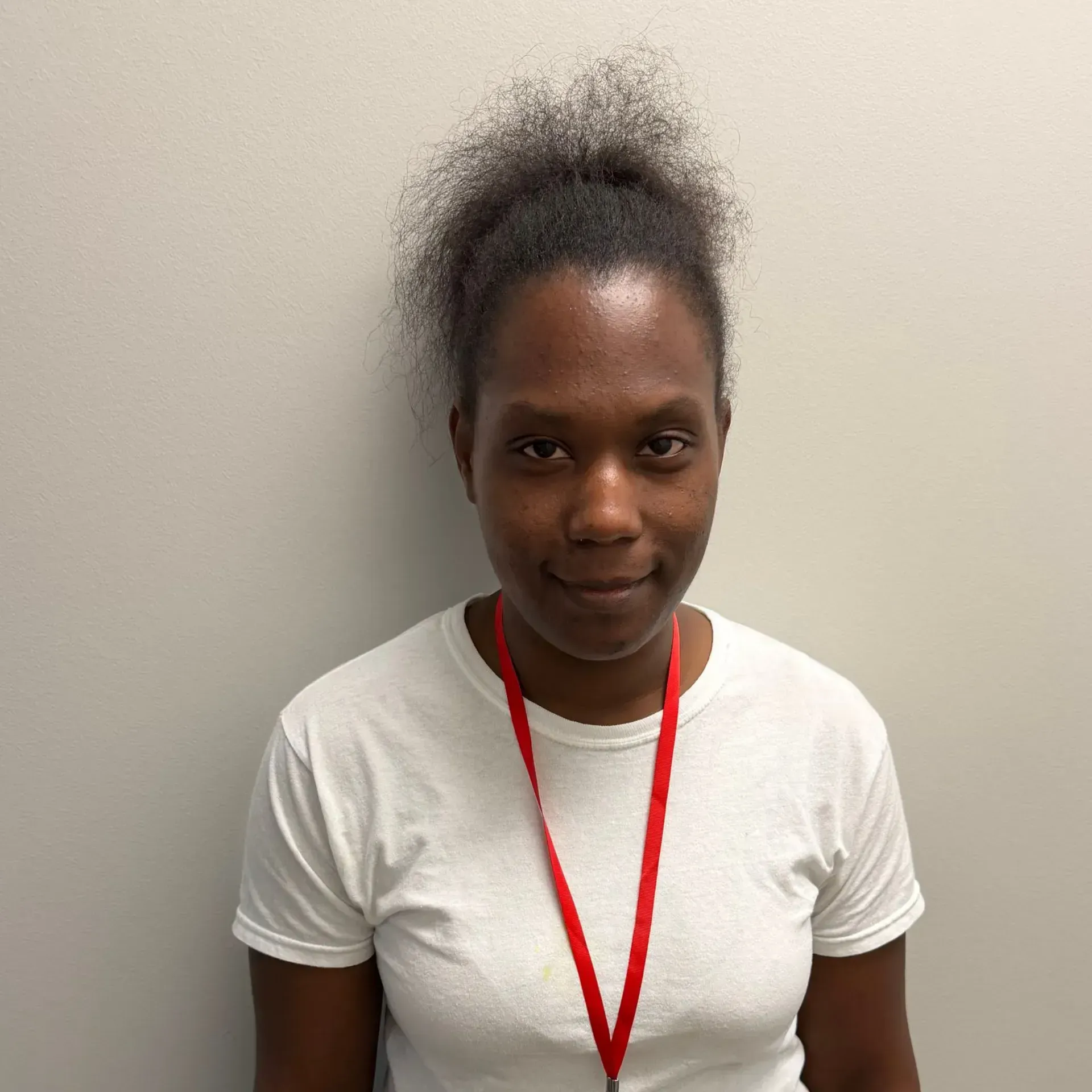 Person wearing a white t-shirt and red lanyard stands against a gray wall.